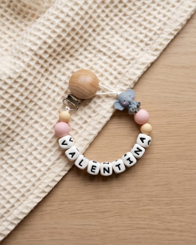 Chupetero rosa con el nombre VALENTINA y charm de elefante sobre una manta de nido de abeja
